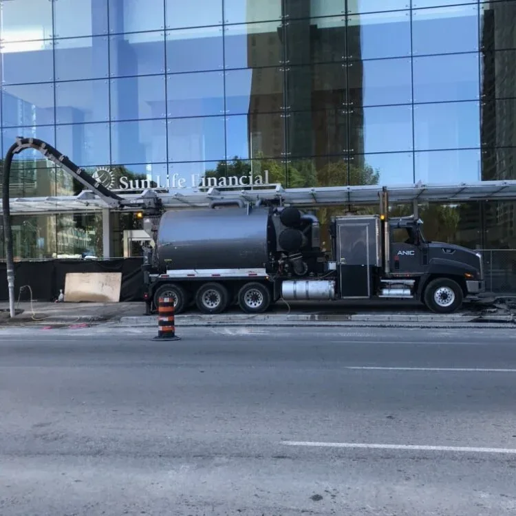 Black ANIC CAT hydro vac truck with boom raised working outside the Sun Life Financial tower in downtown Toronto