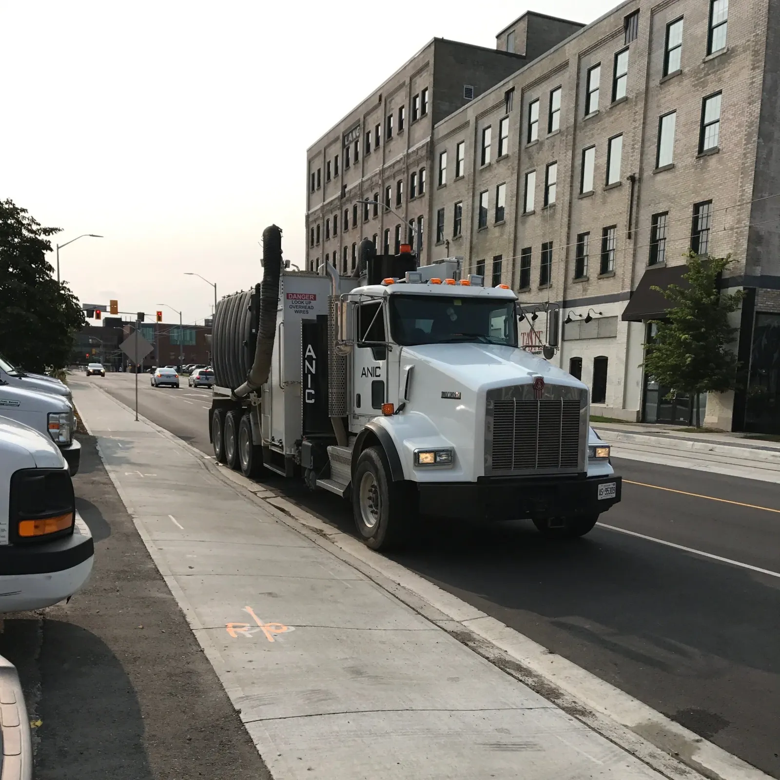 White ANIC Kenworth hydro vac truck parked streetside in a brick warehouse district with fresh locate markings on the sidewalk
